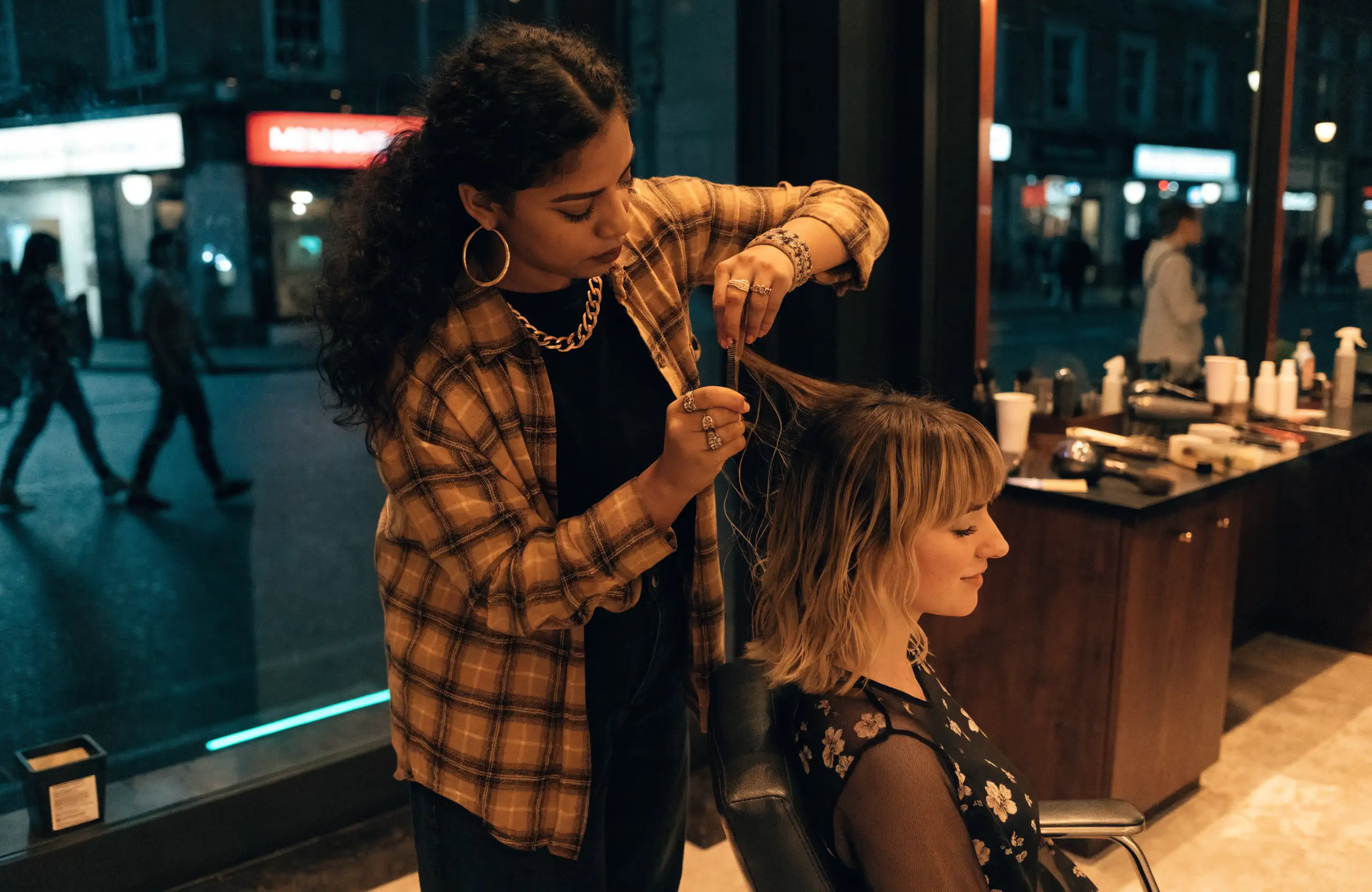 Stylist finishing a client’s hair in a salon in the evening, the street glowing outside